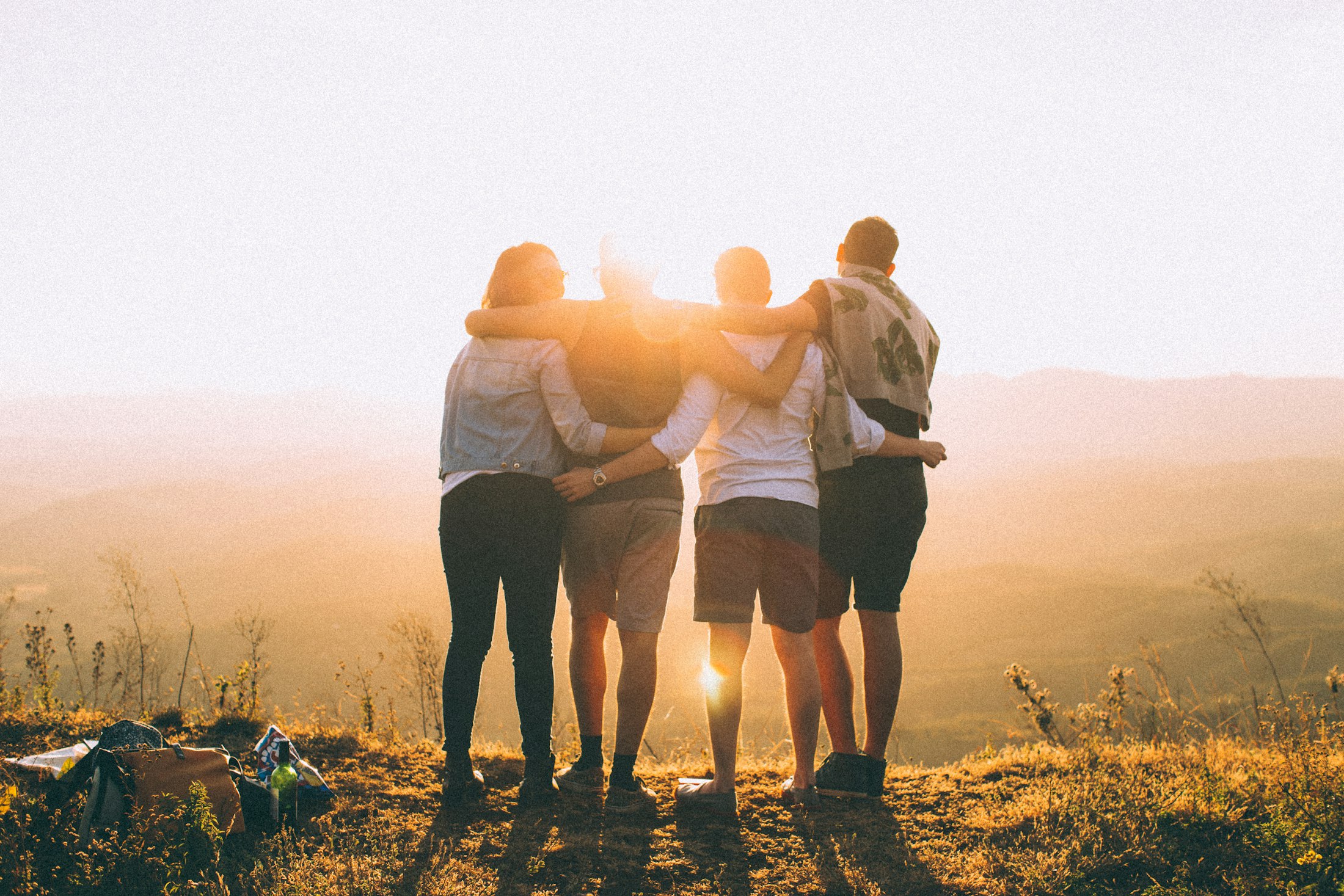 Group of friends with arms around shoulders watching the sunset, symbolizing community and togetherness